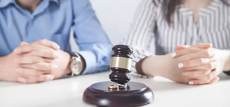 A photo of a judge's gavel resting on top of a pair of wedding bands with a man and woman in the background.