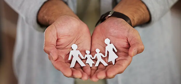A photo of a person holding a paper cutout of a family in the palm of their hands.