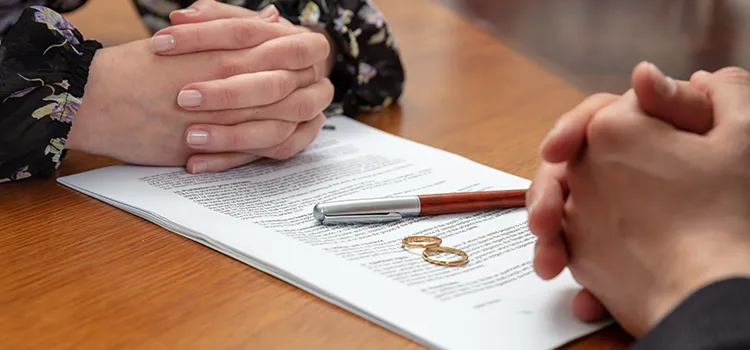 Two individuals with their hands folded over a legal document with 2 wedding rings atop it.