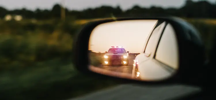A photo of a police car with its lights flashing in a driver's side view mirror.