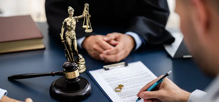 A photo of a man signing a legal document next to a gavel as a judge watches on.