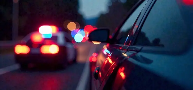 A photo of a car pulled over on the side of the road by a police officer at night.